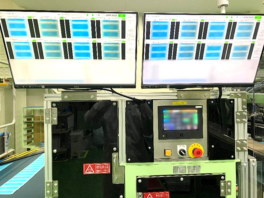 製造ラインの検査工程で、複数のモニターに表示された画像診断カメラの映像を用いて、『熱さまシート』に不具合がないかを1枚ずつ確認している検査設備の様子