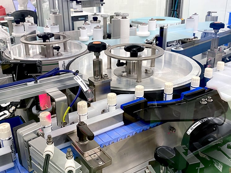 製造ラインで小型容器を搬送しながら充填やキャップ装着を行う装置の様子。回転テーブルとコンベアで連続的に処理されている。