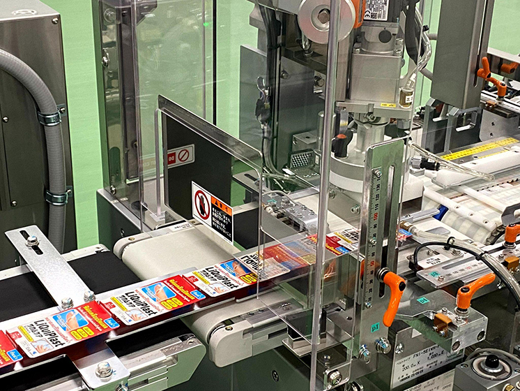 製造ラインで製品パッケージを搬送しながら印刷や貼付を行う装置の様子。ベルトコンベア上で連続的に処理されている。