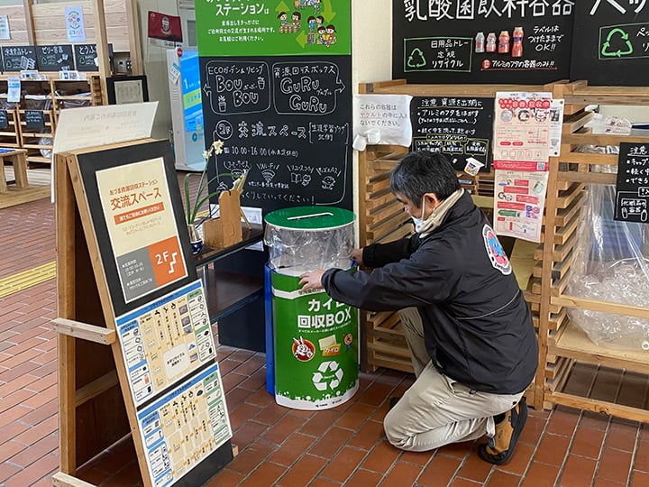 施設内で男性が「カイロ回収BOX」設置している様子。背景にはリサイクルステーションの案内や掲示物がある。