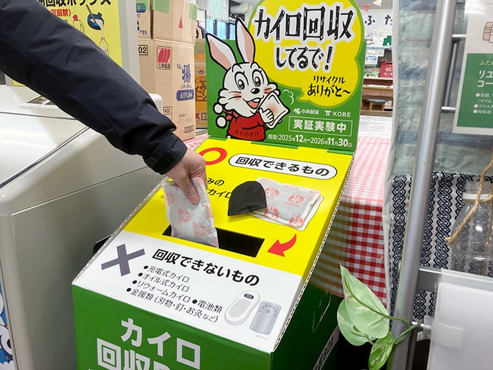使用済みカイロの回収ボックスに手で投入している様子。『カイロ回収してるで！』と書かれた案内と、回収できるもの・できないものの説明が表示されている。
